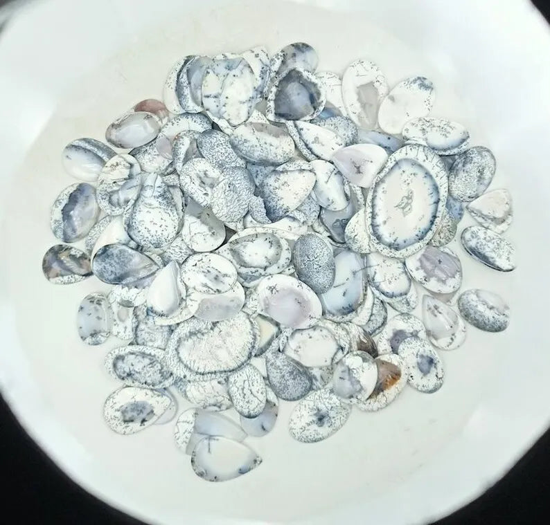 Pile of oval dendrite opal cabochon stones, white with black speckles