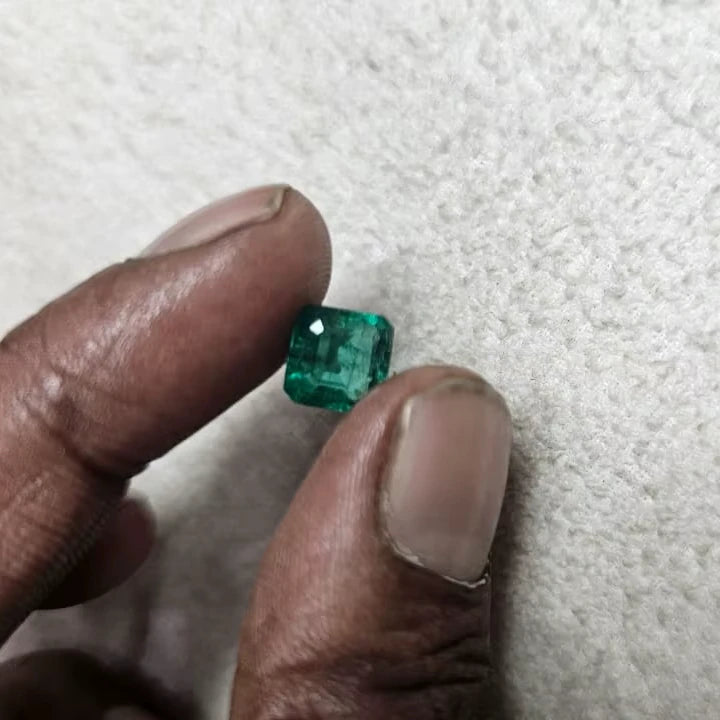 Green emerald-cut gemstone held in fingers, small rectangular cut on felt