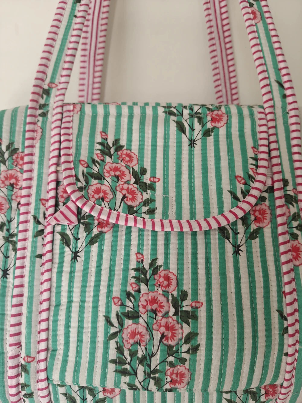 Luxury quilted weekender bag with light green stripes, pink floral print, and striped trim. Artisan designer handbag.