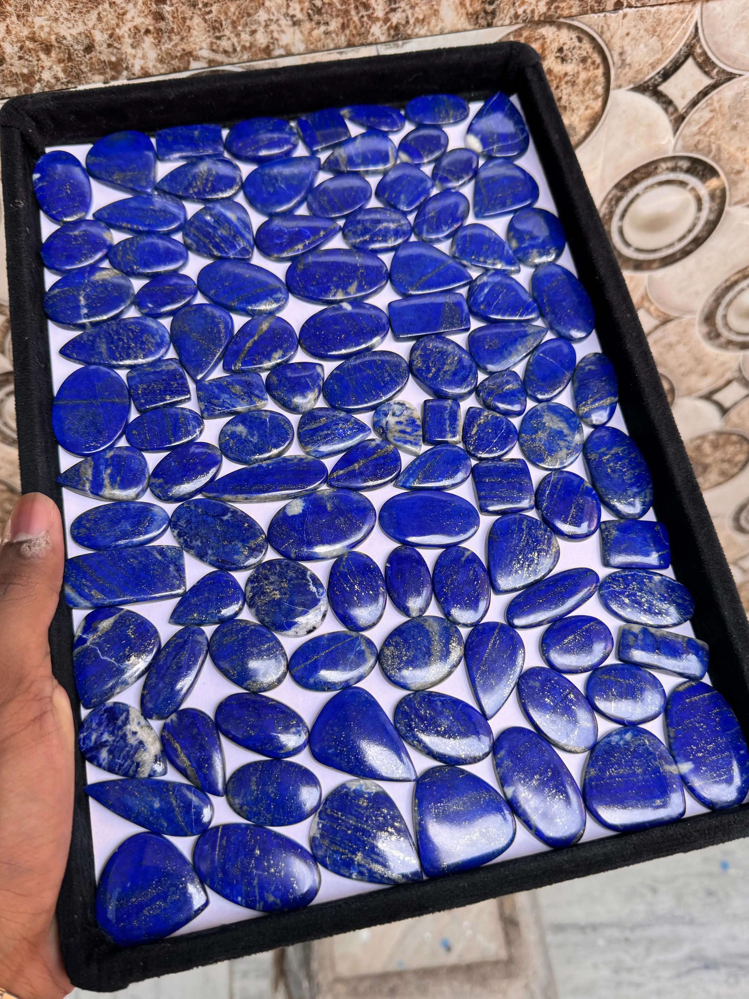 Lapis lazuli cabochon gemstone assortment in a black tray, blue ovals and rounds