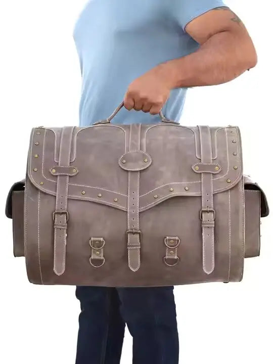Large grey leather trunk bag with vintage buckle straps, brass stud detailing, and side pockets for men's travel.