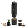 Portable black espresso maker for capsules and ground coffee with integrated cup on white background.