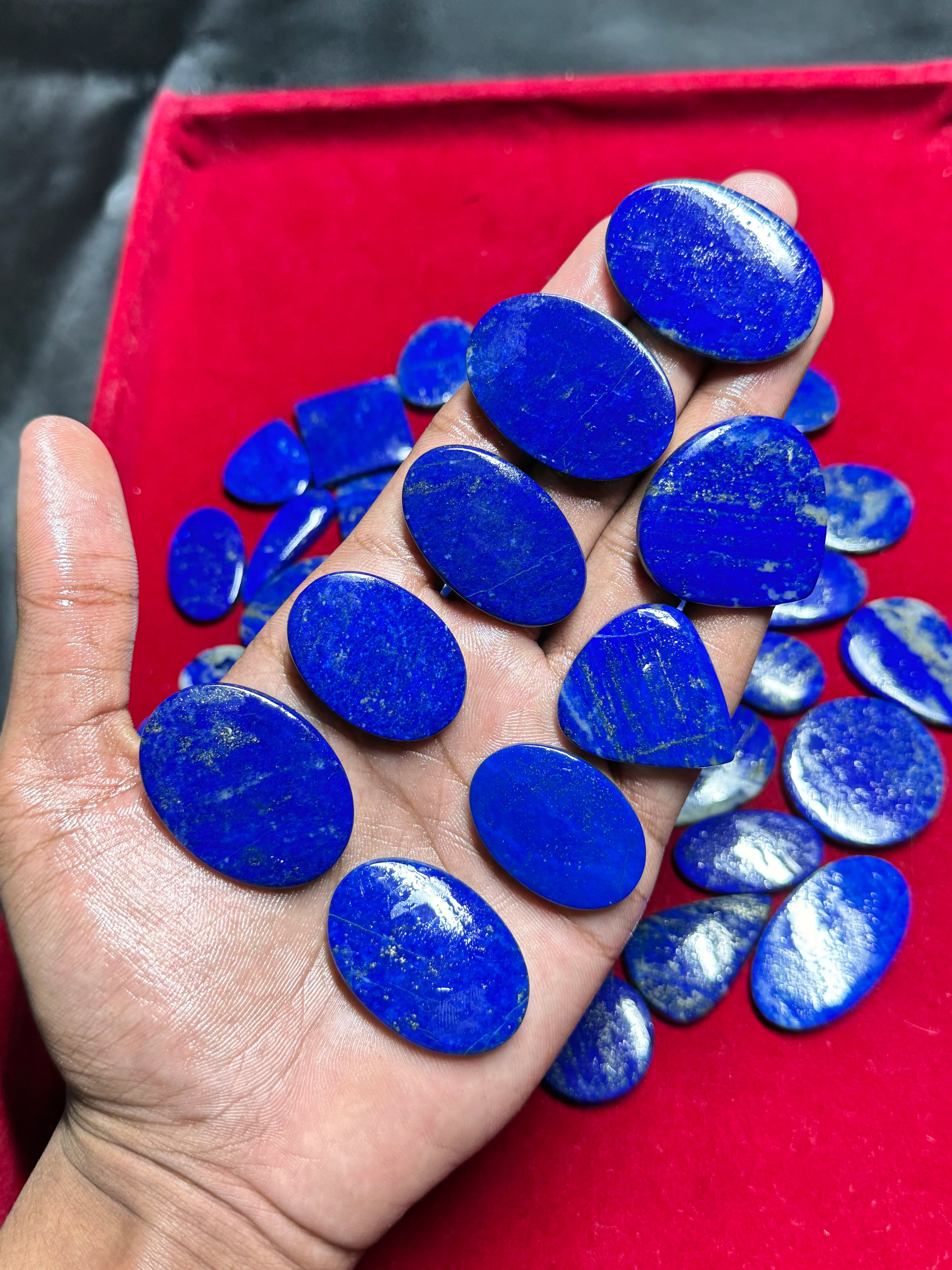 Smooth blue lapis lazuli cabochon gemstones, blue ovals in palm, loose pieces