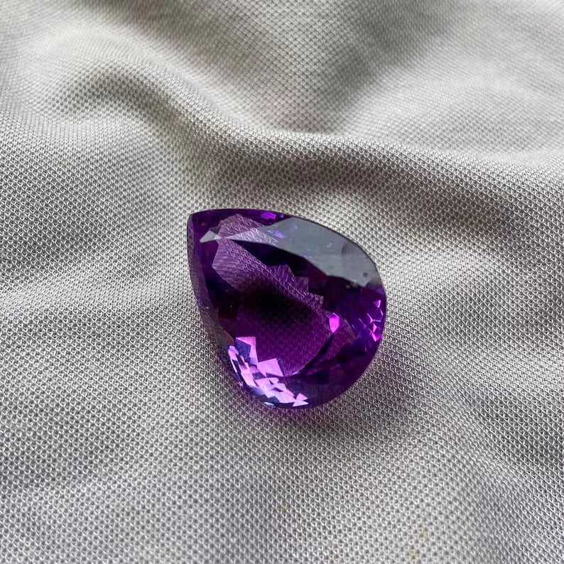 Amethyst gemstone pear cut with angled facets creating bright purple light flashes