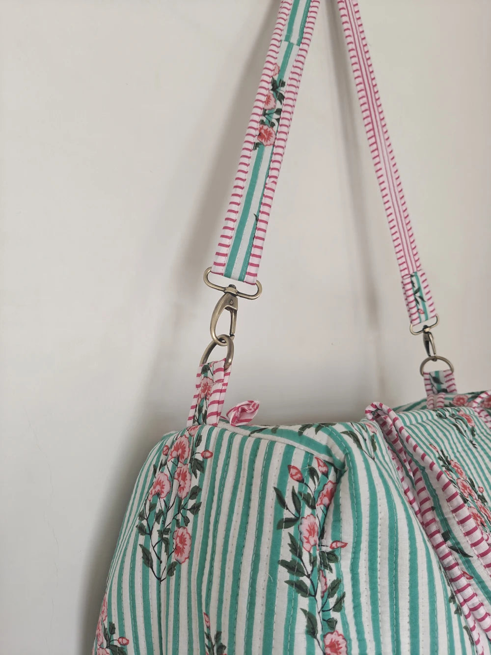 Quilted weekender duffle bag in light green stripes and pink floral print with adjustable striped artisan shoulder strap.