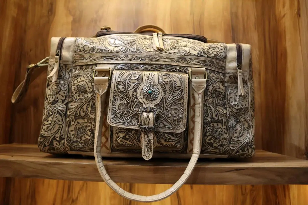 Handmade vintage Western brown cowhide travel duffel with floral tooling, turquoise concho, and antique finish.