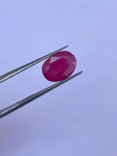 Oval faceted red gemstone on metal tweezers, angled view