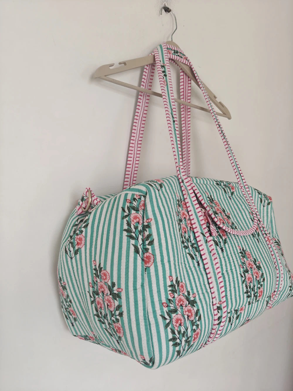 Vintage-style quilted weekender duffle bag in light green stripes with a floral print and vibrant pink accents.
