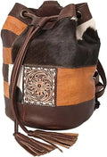 Western bucket bag in patchwork leather and cowhide with tooled floral detail, drawstring closure, and tassel accents.