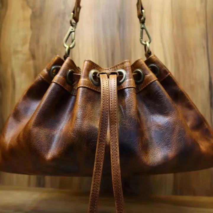 Distressed brown leather bucket bag with drawstring closure, metal grommets, and detachable shoulder strap. Trunk style.