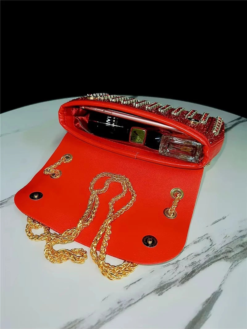 Red leather crossbody trunk purse with gold chain strap, rhinestone detailing, and magnetic clasp closure.