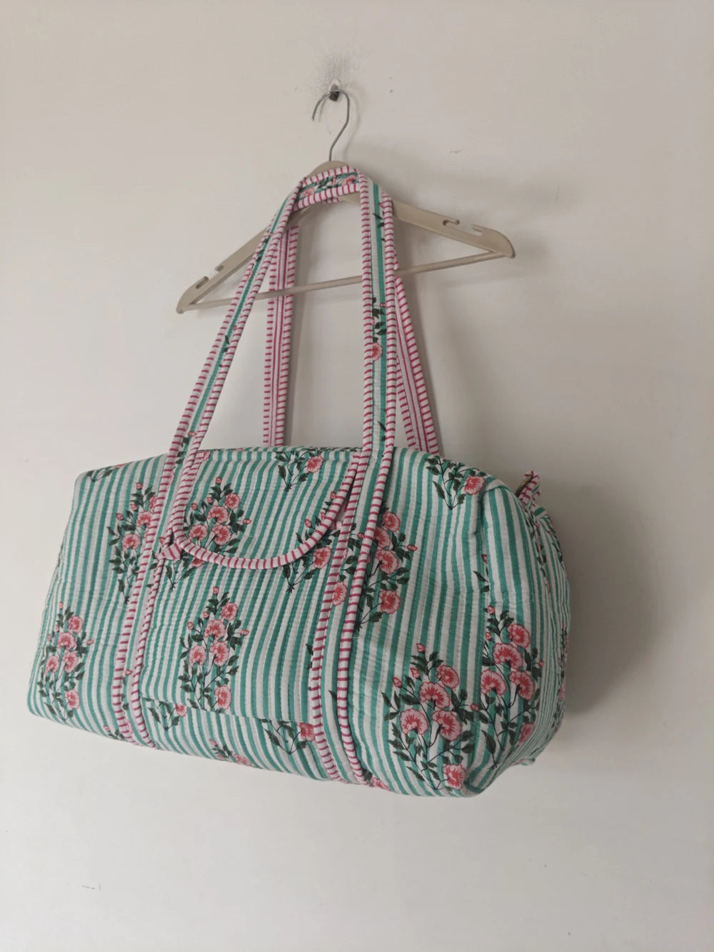 Quilted designer weekender duffle in light green striped fabric with pink floral patchwork and sturdy carrying straps.