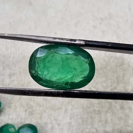 Large green oval gemstone held in tweezers over felt