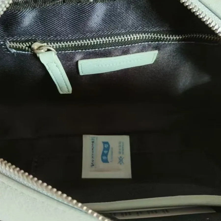 Mint green trunk tote interior with zipper pocket, leather branding tab, dark fabric lining, and silver hardware.