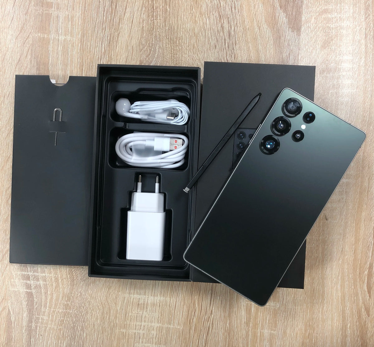 Dark green smartphone with open retail box, charging cable, and wall adapter