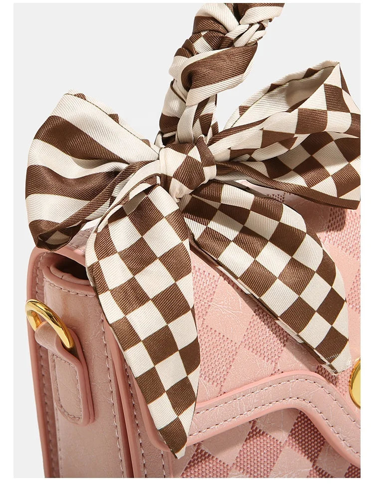 Pink leather trunk handbag with brown and white plaid silk bow, gold hardware, and braided top handle.