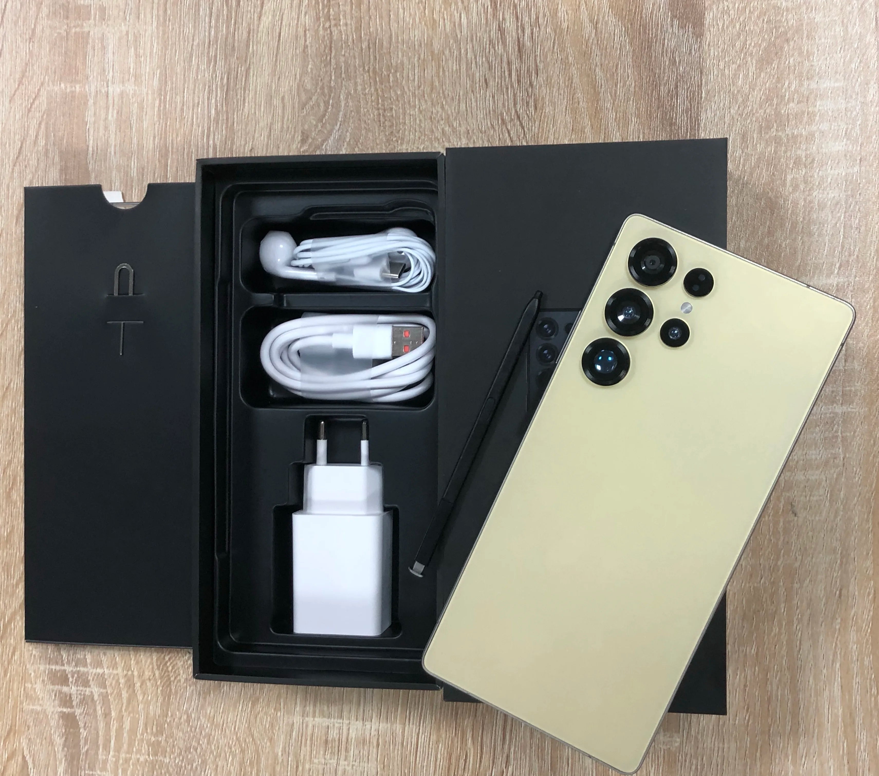 Android smartphone with gold back and quad rear cameras; box with cable and charger