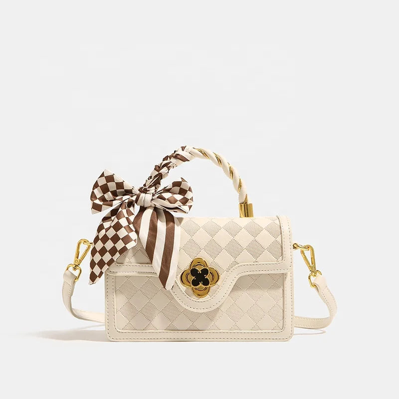 Off-white luxury trunk handbag with quilted plaid pattern, gold flower clasp, twisted handle, and plaid silk scarf.