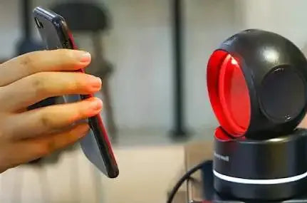 Hand holding a barcode scanner next to a black Honeywell USB stand with red ring