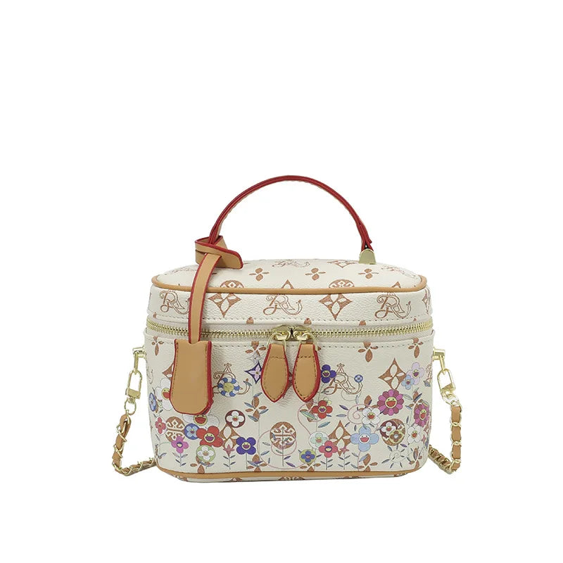 Cream genuine leather trunk bag with floral pattern, red handle, gold hardware, and detachable chain crossbody strap.