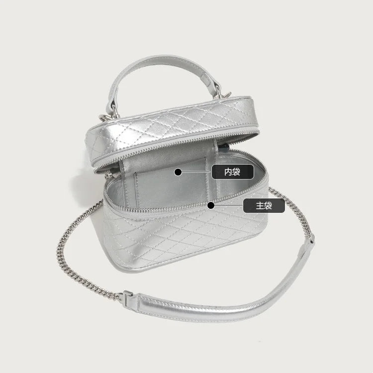 Silver quilted leather trunk bag with top handle, zipper closure, and removable chain crossbody strap for women.