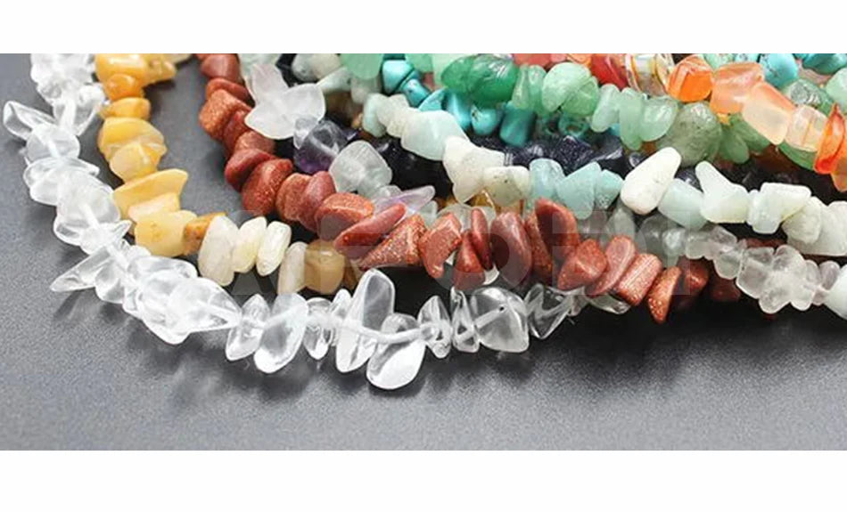Strands of multicolored, irregular raw gemstone chips for jewelry making, arranged in a layered curve.