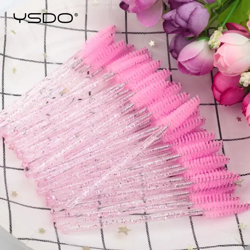 Disposable eyelash brushes with pink bristles and clear, glitter-filled plastic handles for lash and brow grooming.
