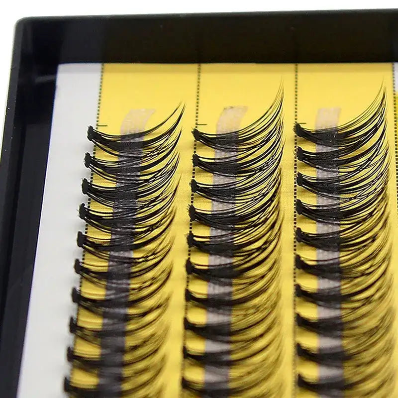 Black, curled Russian volume eyelash clusters arranged in three rows on a yellow adhesive strip in a tray.