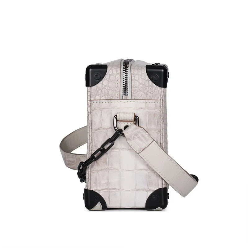White crocodile leather mini trunk handbag with black metal corners and chain strap detail.