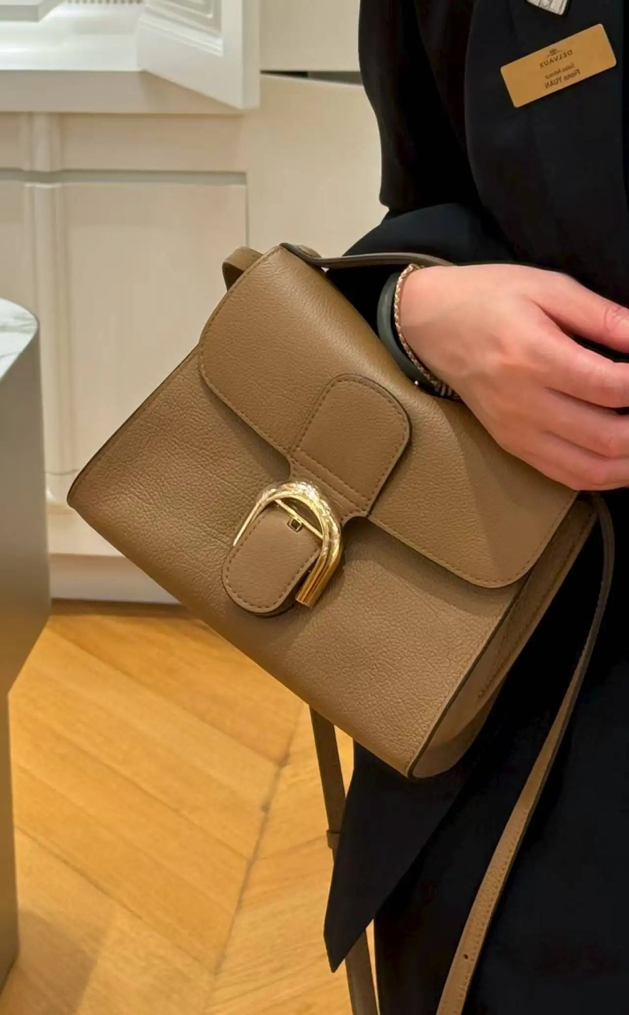Taupe pebble leather designer shoulder bag with flap closure and gold U-shaped metal buckle. Elegant luxury handbag.