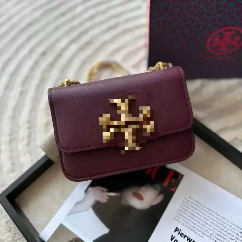 Burgundy leather crossbody trunk bag with gold metal logo hardware and a gold chain shoulder strap.