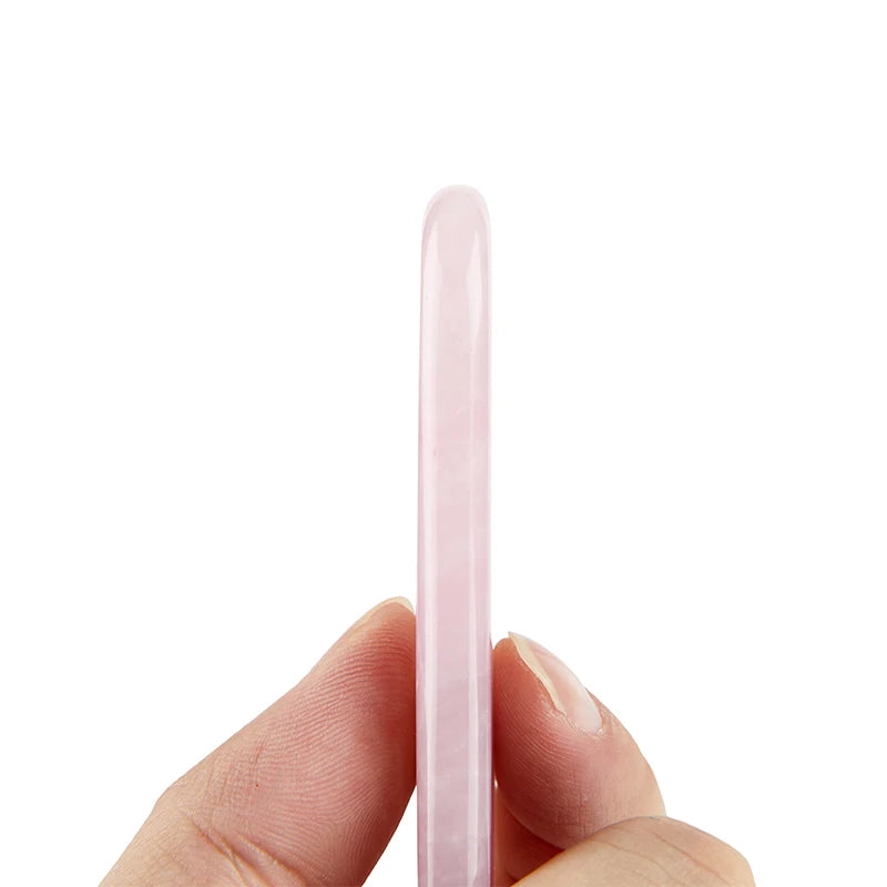 Hand holding a smooth, cylindrical pale pink rose quartz Gua Sha facial massage wand against a white background.