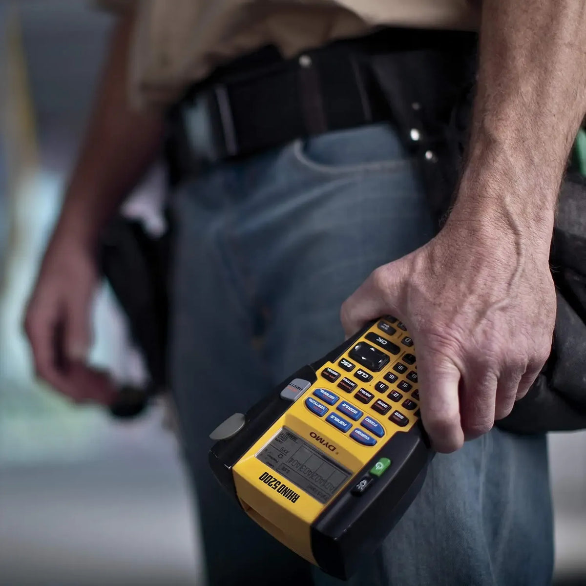 Handheld DYMO label maker applying a label strip to a surface
