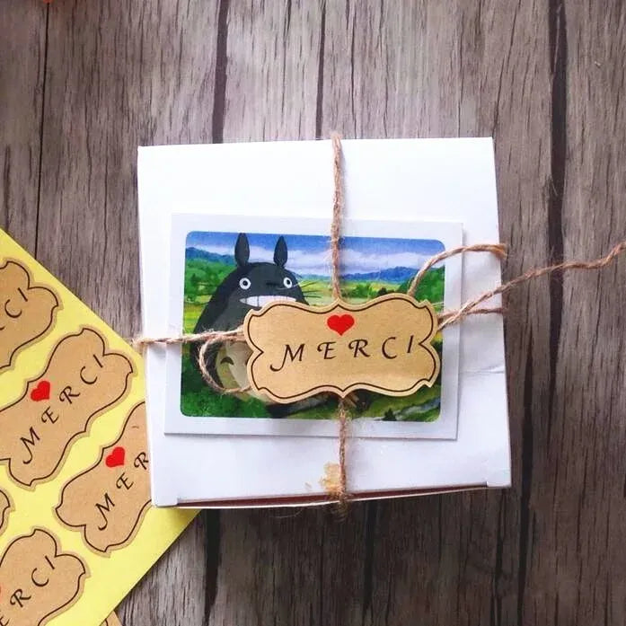 Gift tag label on kraft-style string, flower shape with MERCI text and red heart
