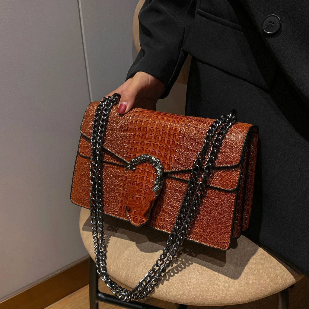 Brown crocodile pattern crossbody bag with a horseshoe clasp and black metal chain strap, luxury style trunk handbag.