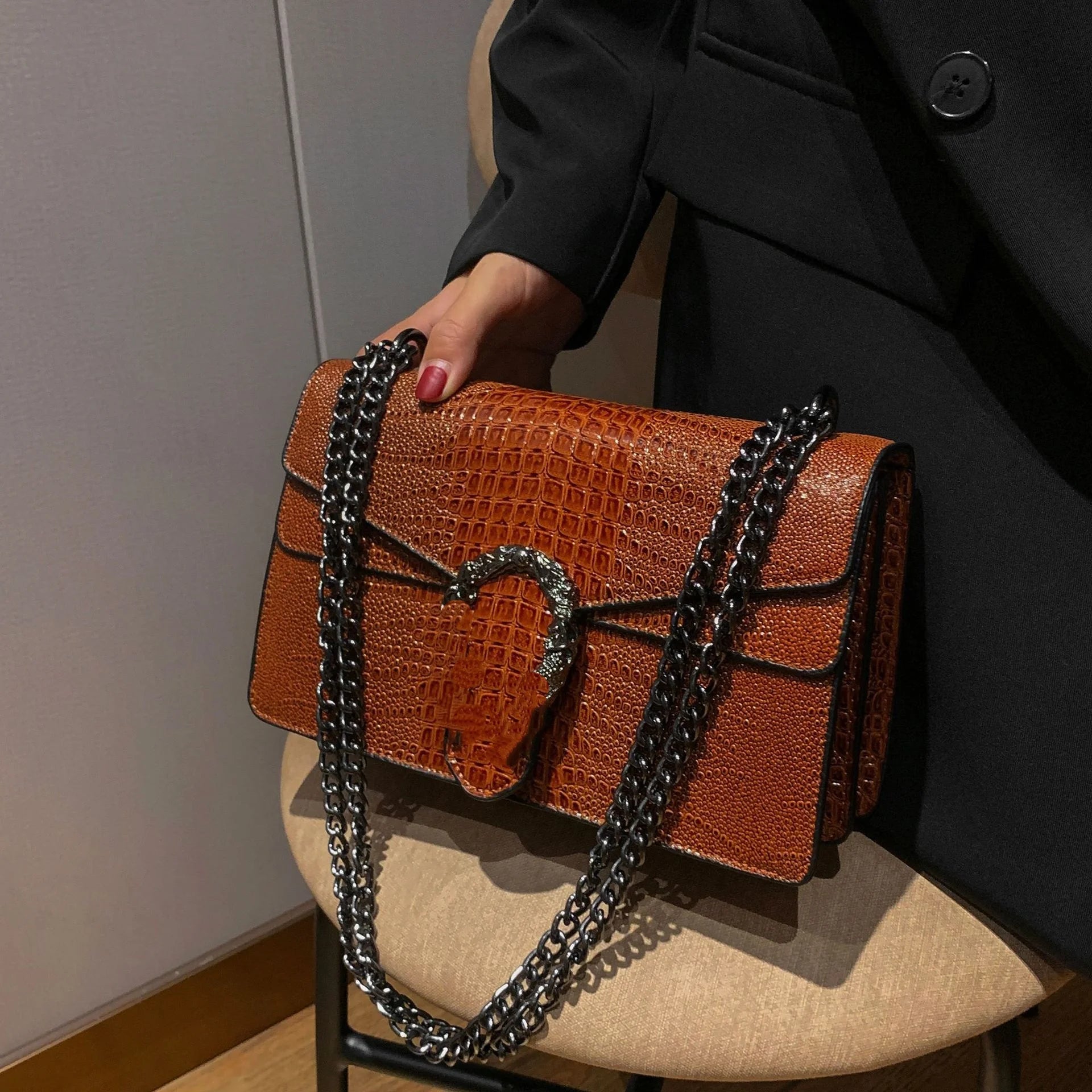Brown crocodile pattern crossbody bag with a horseshoe clasp and black metal chain strap, luxury style trunk handbag.