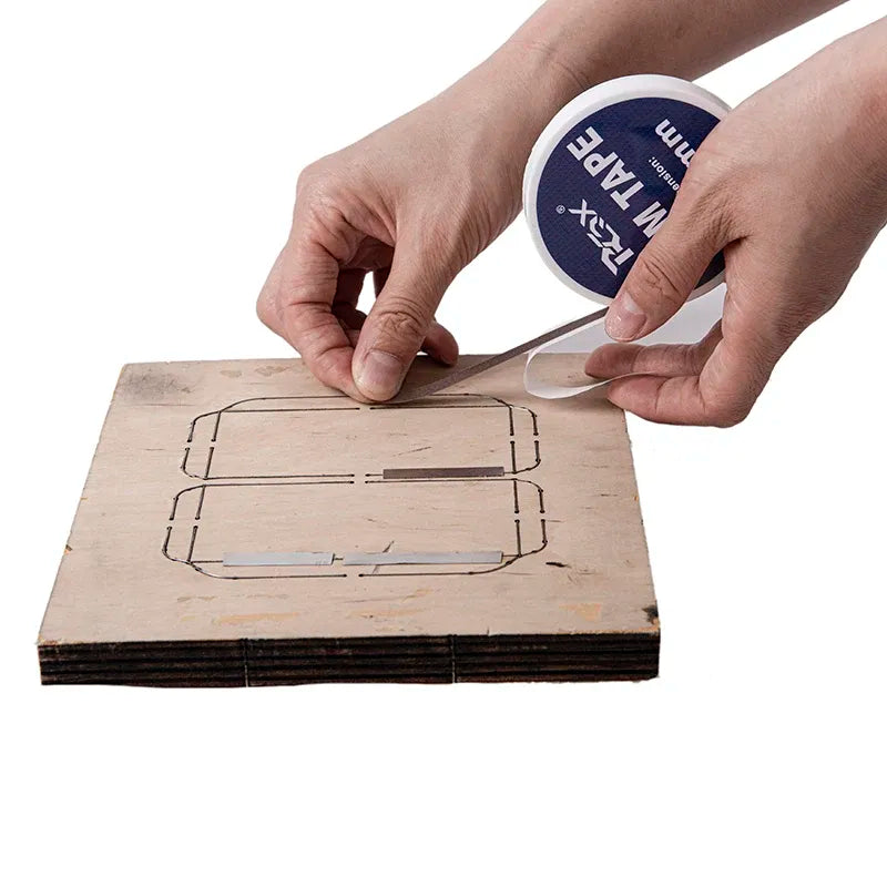 White shim tape roll applying tape along a cut-out template on cardboard