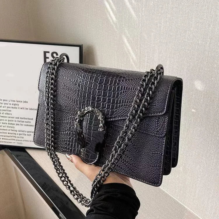 Black crocodile pattern luxury crossbody trunk bag with metallic chain strap and ornate silver horseshoe-style clasp.