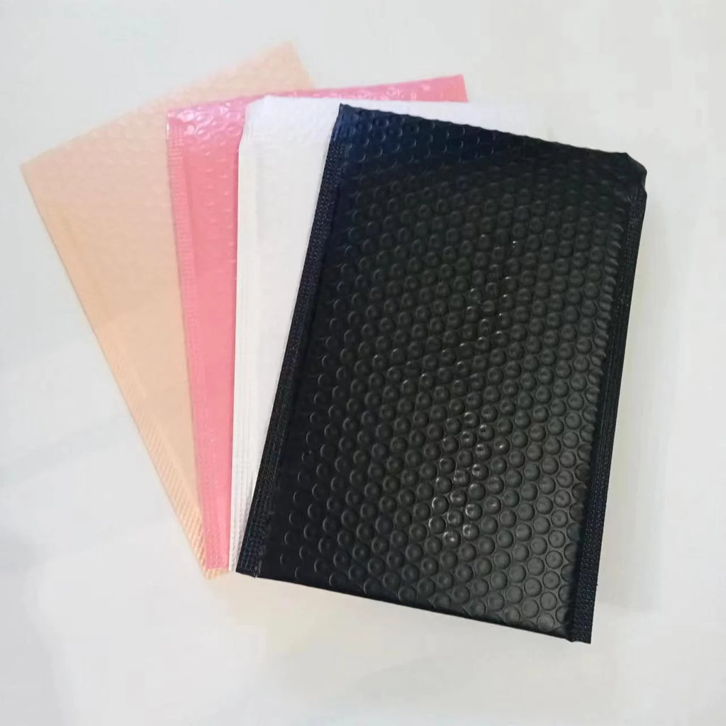 Stack of bubble mailers in black, pink, white, and beige with raised bubble texture.