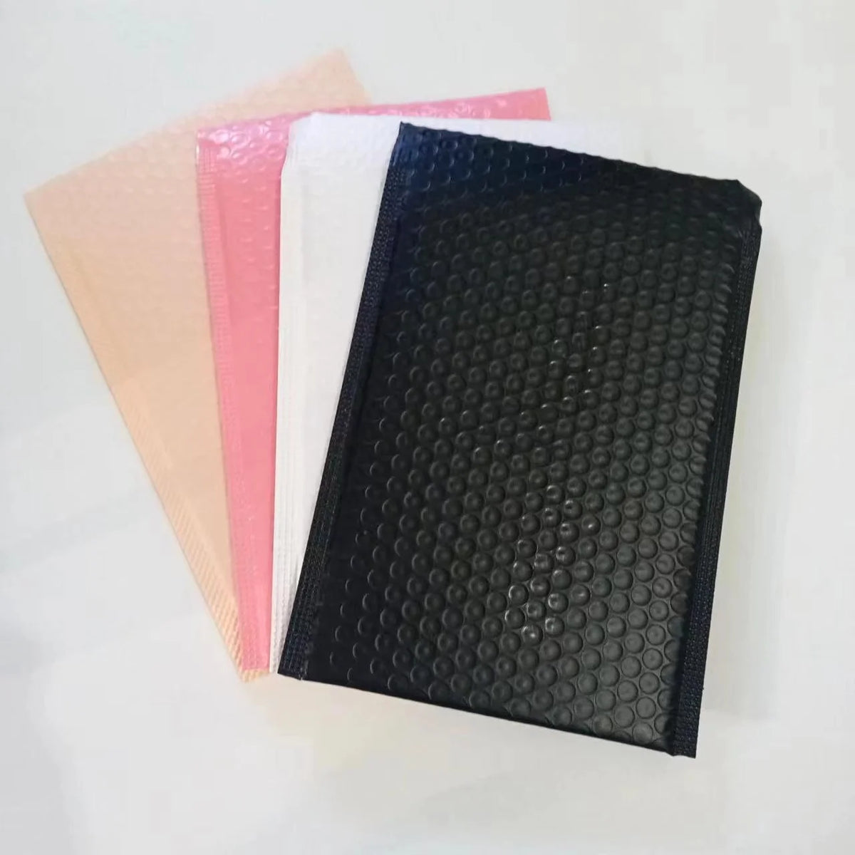 Stack of bubble mailers in black, pink, white, and beige with raised bubble texture.