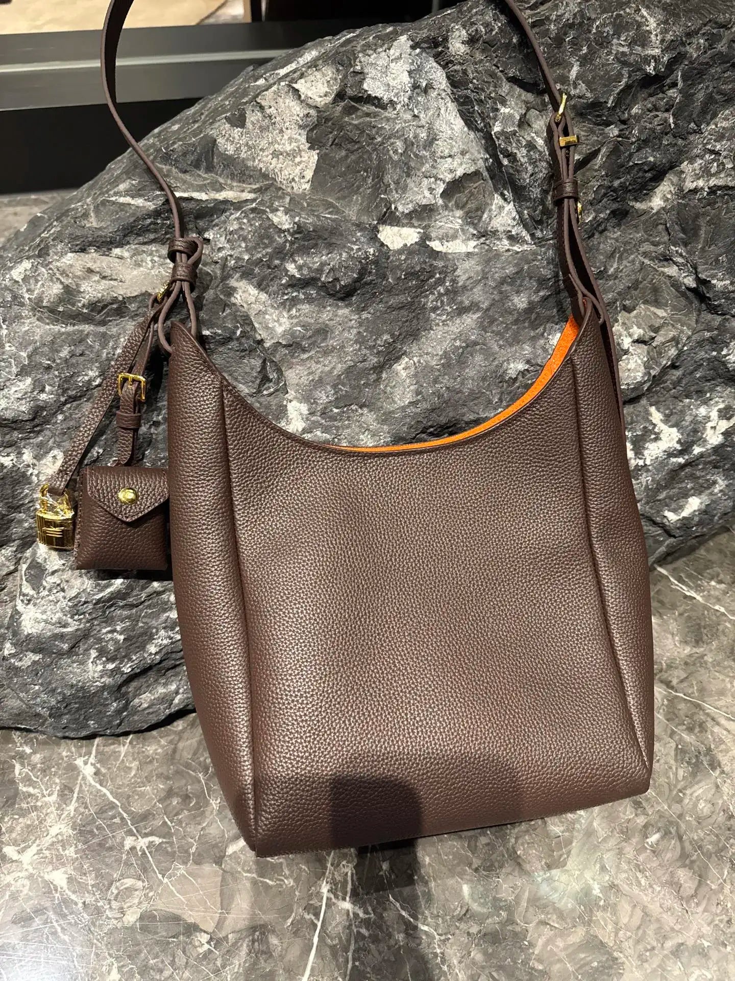 Brown genuine leather hobo shoulder bag with orange interior, adjustable strap, and small hanging charm accessory.