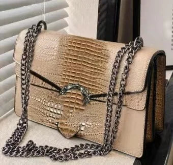 Beige crocodile pattern luxury crossbody bag with dark metal chain strap and decorative buckle for women.