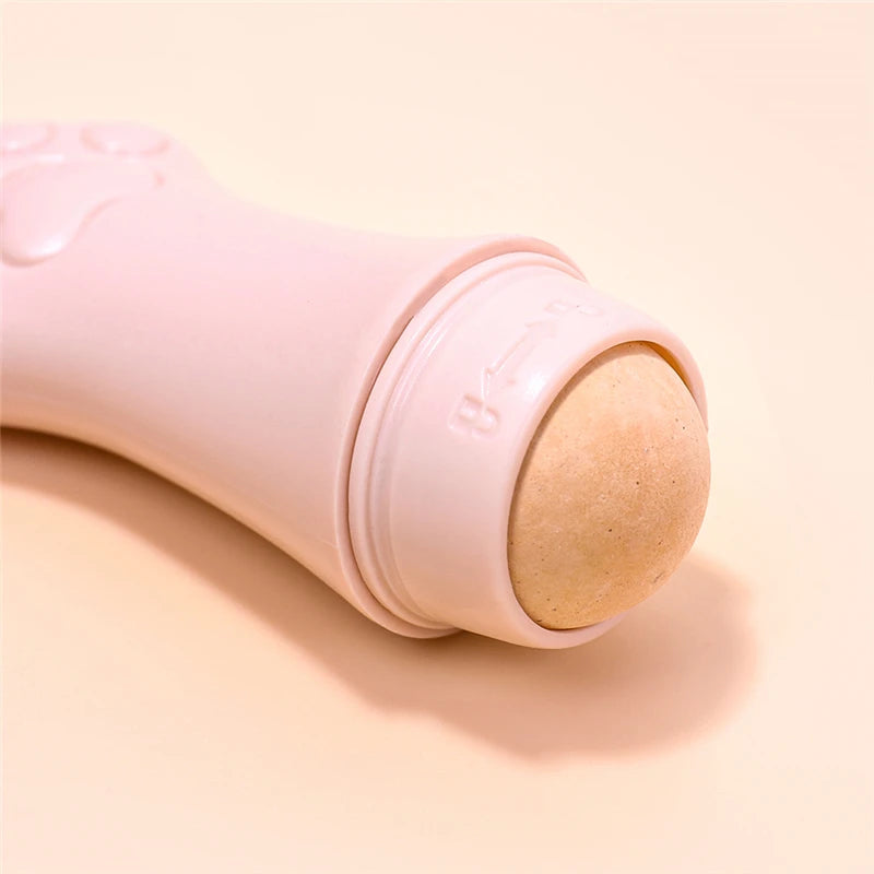 Pink cat paw-shaped face oil absorbing roller with a beige volcanic stone ball, set against a matching light background.