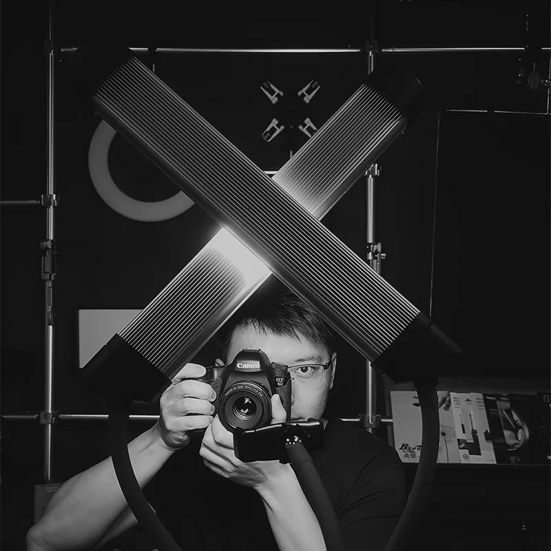 Two black, ribbed LED light bars crossed in an X shape, mounted on flexible arms for studio photography lighting.