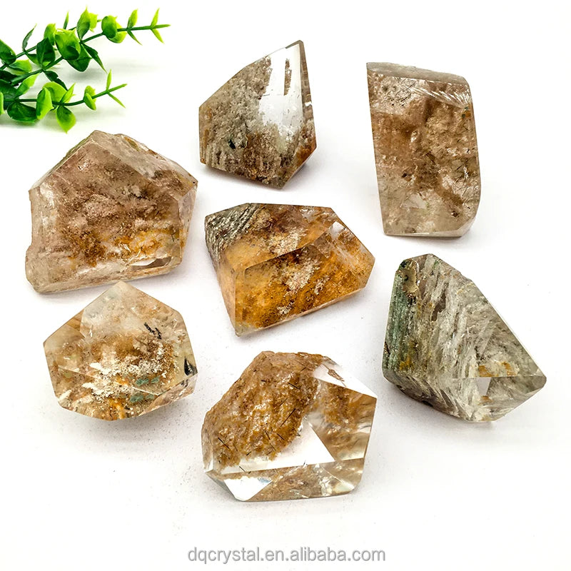 Assorted polished phantom quartz crystals arranged together, clear with brown-gold inclusions