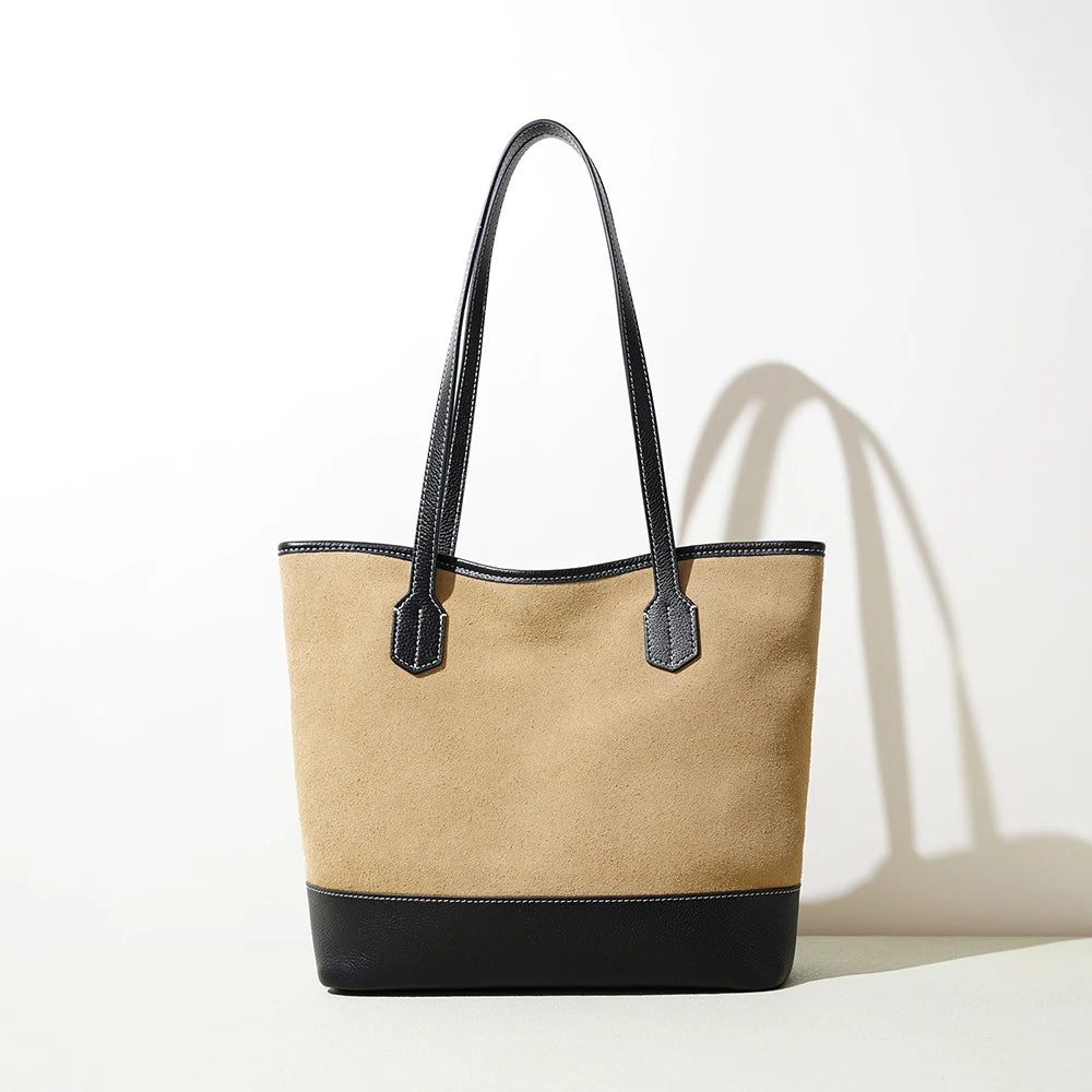 Vintage-style beige suede tote bag with black leather trim, long handles, and minimalist design.