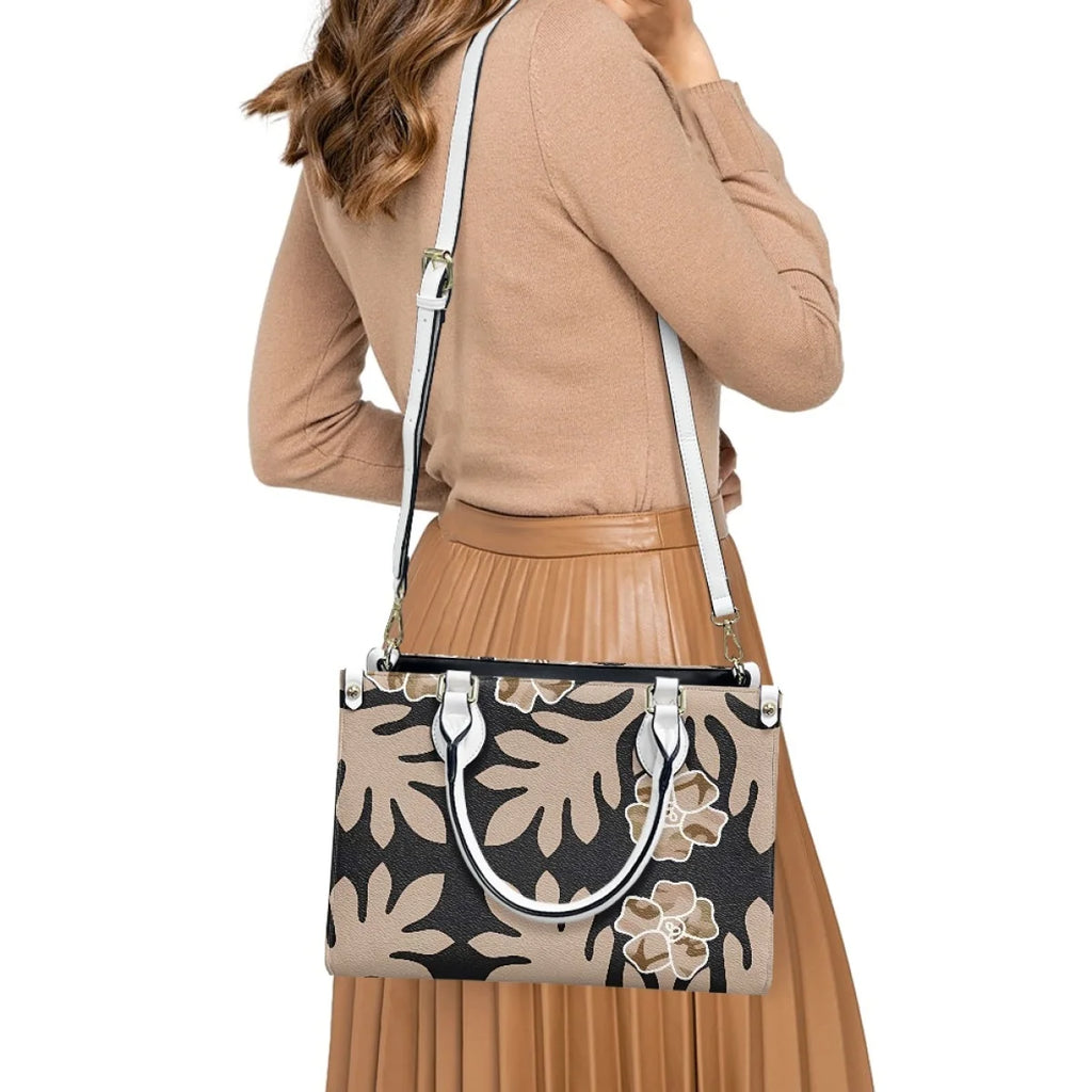 Luxury black and tan Polynesian tribal floral leather handbag with white handles and adjustable shoulder strap.