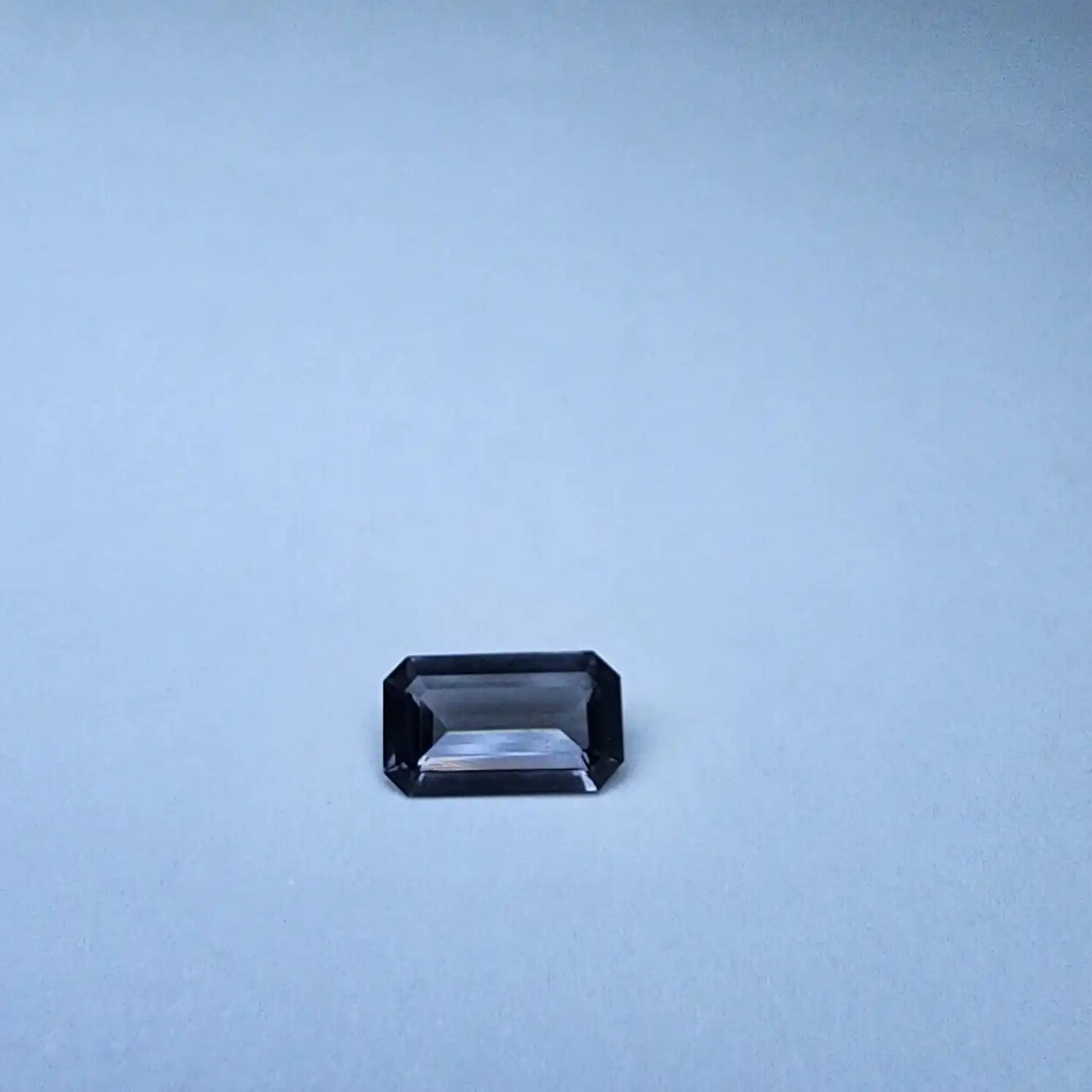 Dark gray emerald-cut spinel gemstone, centered on light background
