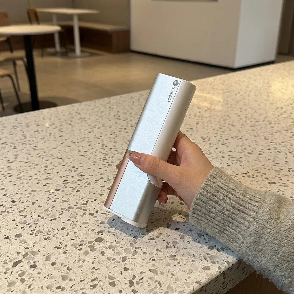 Portable handheld coffee printer, white body held over a countertop