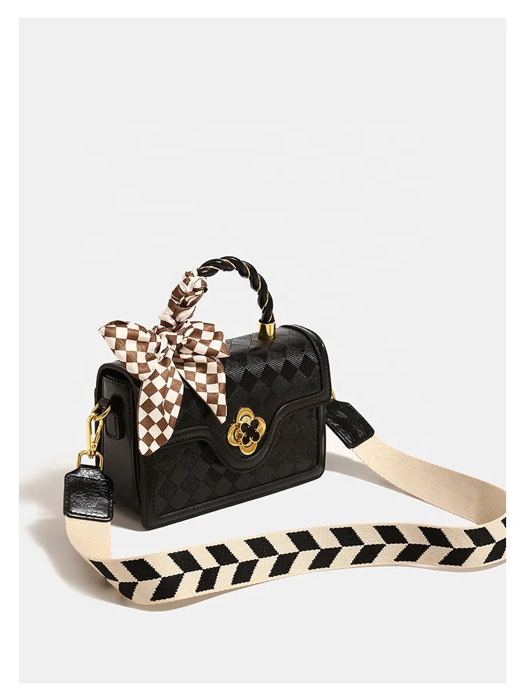 Black plaid leather luxury trunk handbag for ladies with patterned scarf, gold hardware, and wide chevron strap.